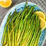 Pinterest graphic of overhead of air fryer asparagus, cooked, on a platter with lemon slices that says: "the best air fryer asparagus simplejoy.com"