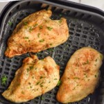 Pinterest graphic of air fryer chicken breasts recipe. Text says, "Air Fryer Chicken Breasts simplejoy.com" Overhead photo of air fryer chicken breasts in air fryer basket