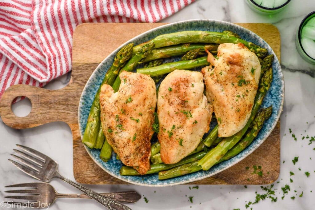 Overhead photo of air fryer chicken breasts recipe served on top of asparagus on a plate.