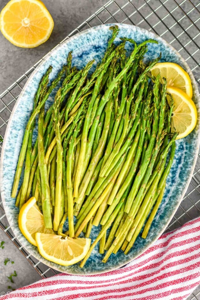 overhead of air fryer asparagus, cooked, on a platter with lemon slices