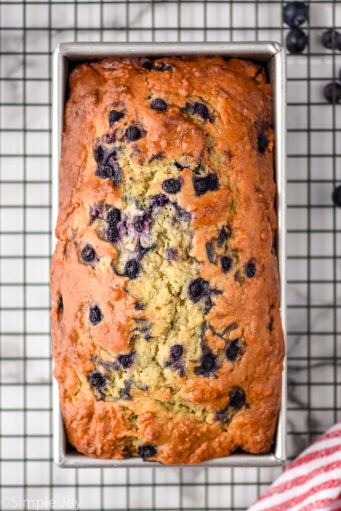 overhead of banana bread with blueberries in a bread pan on a cooling rack