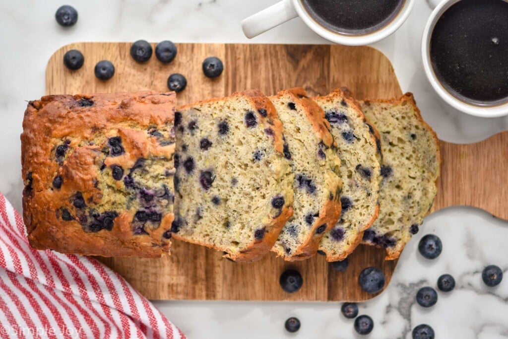 Overhead photo of blueberry banana bread sliced on a wooden cutting board.