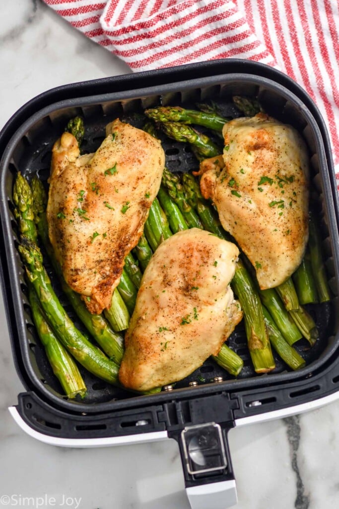 Overhead photo of air fryer chicken breasts in air fryer basket on top of asparagus