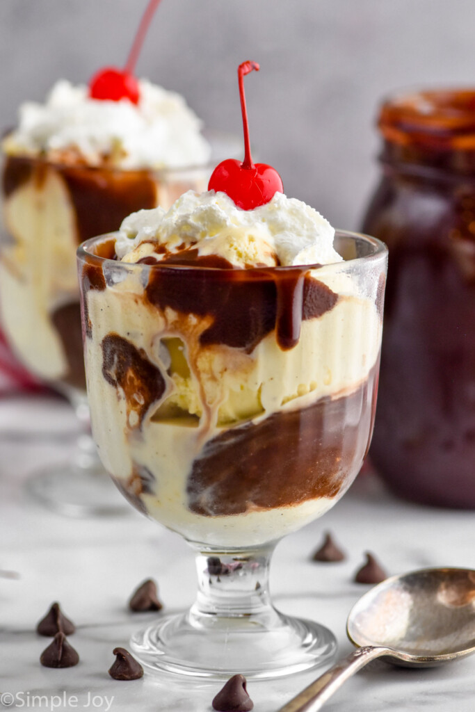 a hot fudge sundae in a glass with whipped cream and a cherry