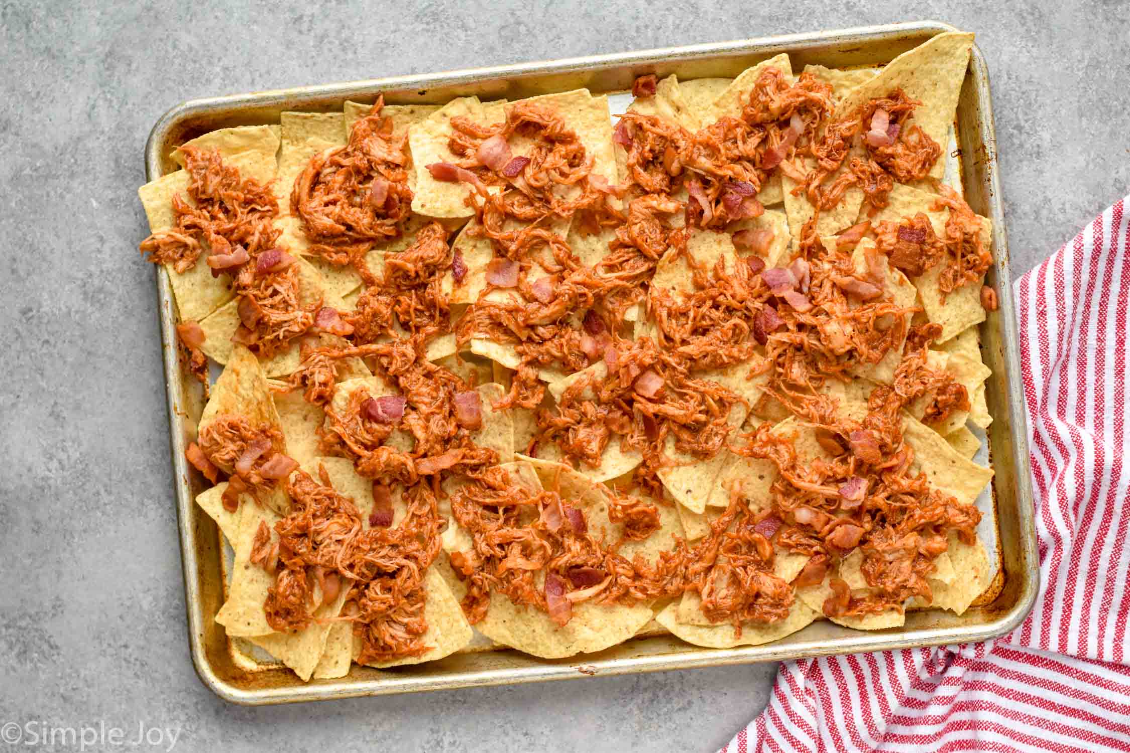 rimmed baking sheet with tortilla chips, bbq chicken, and bacon