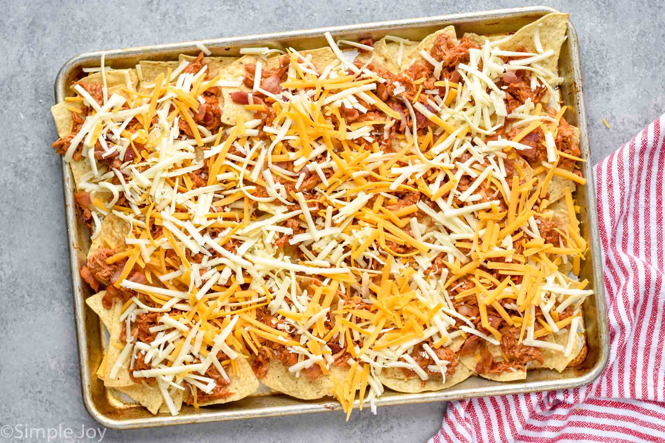 a rimmed baking sheet with tortilla chips, bbq chicken, and shredded cheese