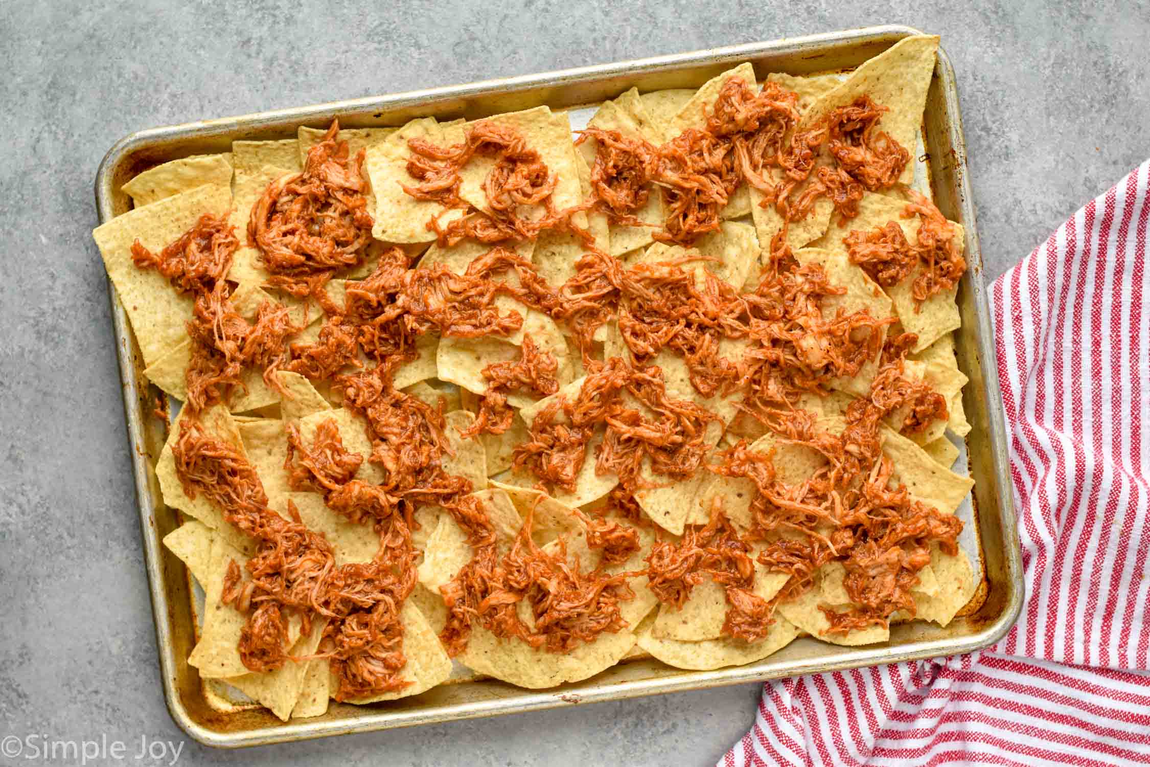 overhead photo of a rimmed baking sheet with tortilla chips and bbq chicken on top