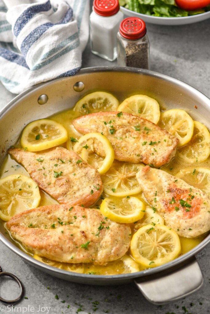 side view of a skillet with chicken and lemons in a buttery sauce