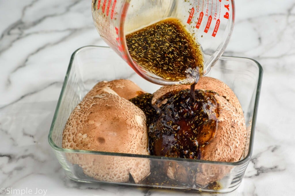 four portobello mushroom caps in a shallow dish with marinade being poured over them