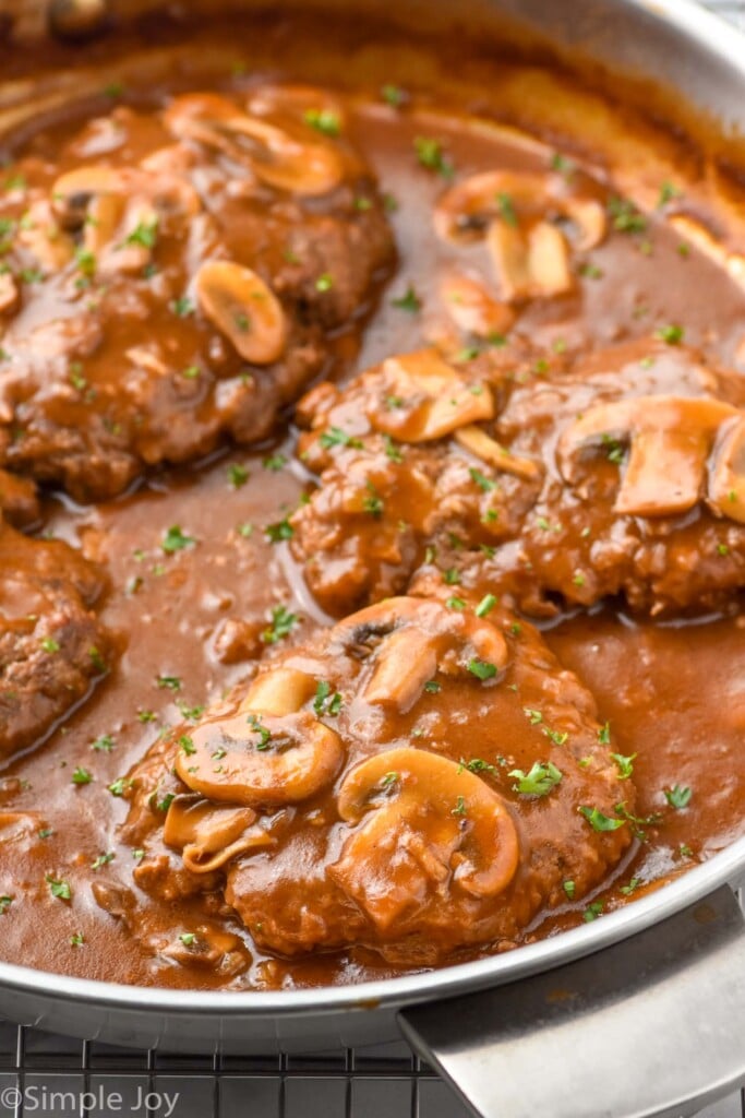 side view of a Salisbury steak recipe in a pan with gravy, garnished with parsley