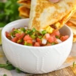 Pinterest graphic of breakfast quesadilla recipe. Image is photo of man's hand dipping a slice of breakfast quesadilla into a small bowl of pico de gallo. Text says, "Super easy breakfast quesadilla simplejoy.com"