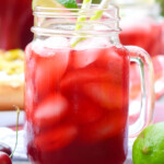 a mason jar glass filled with cherry limeade and ice, garnished with a lime wedge