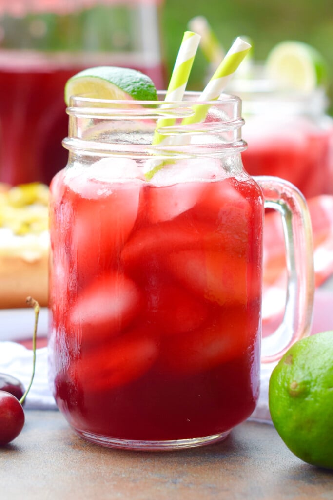 a mason jar glass filled with cherry limeade and ice, garnished with a lime wedge
