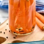 Pinterest graphic of pickled carrots recipe. Sealed Mason jar of pickled carrots sitting on a wooden cutting board. Text says, "Pickled Carrots simplejoy.com"