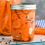 Pinterest graphic of pickled carrots recipe. Sealed mason jar filled with diced pickled carrots sitting on counter top with large jar of whole pickled carrots behind it. Text says, "Pickled Carrots simplejoy.com"
