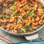 Pinterest graphic of shrimp and broccoli stir fry recipe. Overhead photo of shrimp and broccoli stir fry in a stainless steel pan. Bowl of white rice beside the pan. Text says, Shrimp and broccoli simplejoy.com