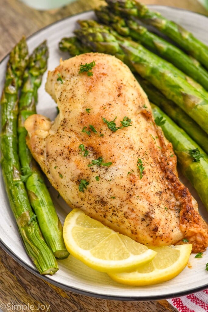 Overhead photo of air fryer chicken breast served on a plate with asparagus and garnished with a fresh lemon wedge
