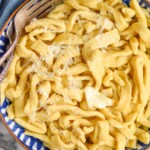 overhead of a bowl of homemade egg noodles, cooked, with butter, seasoning and shredded parmesan cheese on it
