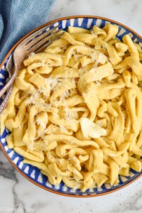 overhead of a bowl of homemade egg noodles, cooked, with butter, seasoning and shredded parmesan cheese on it