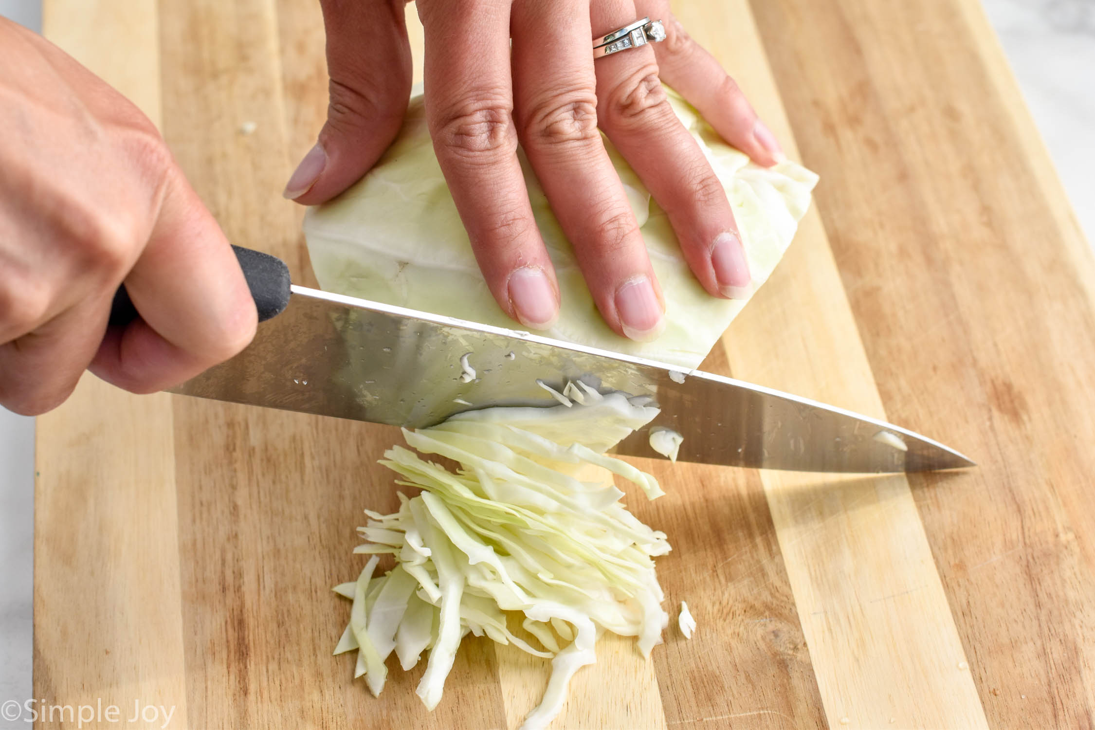 close up picture of a hand holding down a quarter of a cabbage head and cutting thin strips from front to back