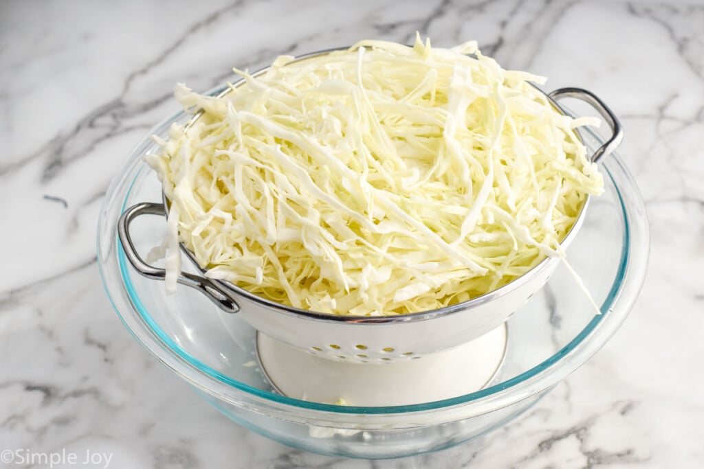 shredded coleslaw in a colander inside a big glass bowl