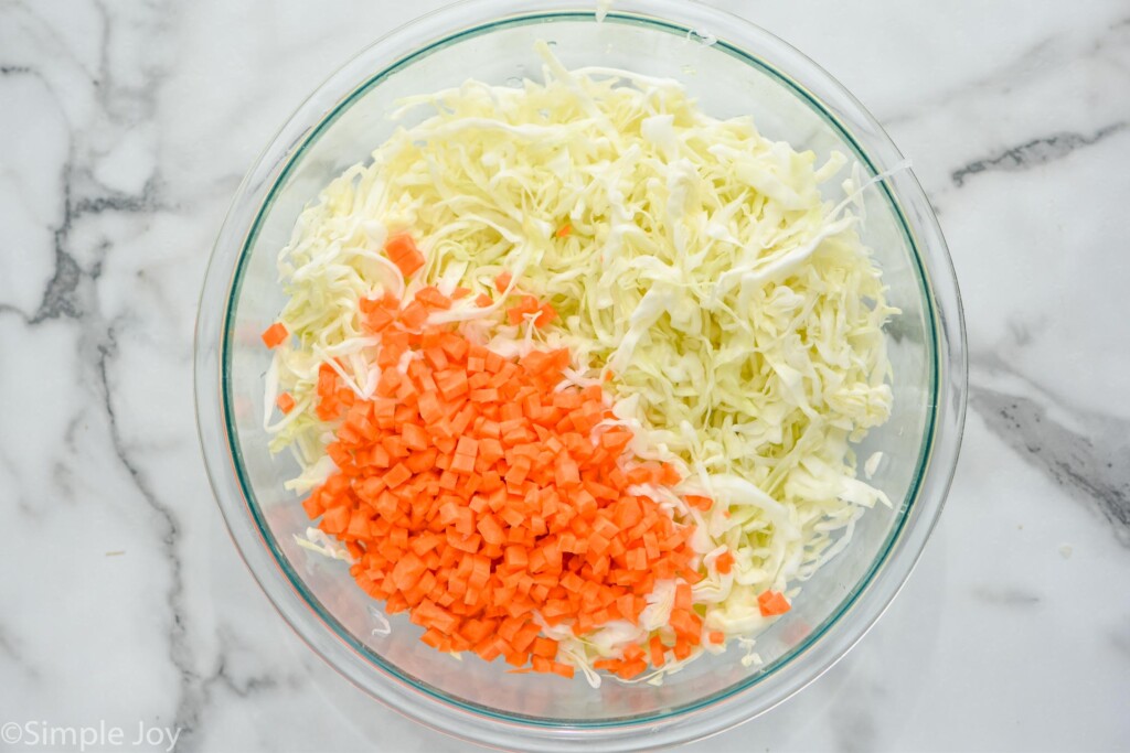 overhead of a bowl of shredded cabbage and diced carrots to make coleslaw recipe