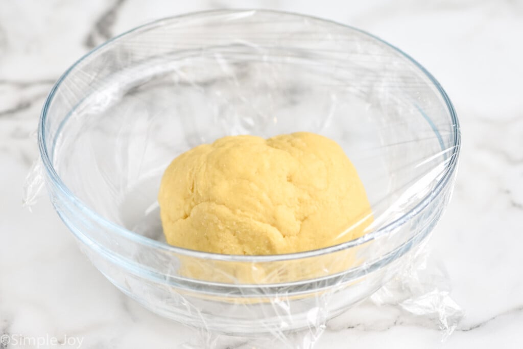 egg noodle dough as a ball in a clear bowl covered in plastic wrap