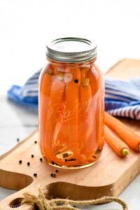Overhead photo of pickled carrots recipe. Sealed Mason jar of pickled carrots sitting on a wooden cutting board.