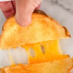 Pinterest graphic of air fryer grilled cheese recipe. Text says, "air fryer grilled cheese simplejoy,com." Overhead photo of man's hand pulling apart two halves of air fryer grilled cheese.