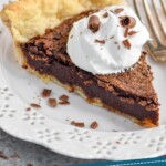 Pinterest graphic of chocolate chess pie recipe. Photo shows a slice of pie garnished with a dollop of whipped cream, served on a plate with a fork resting beside it. Text says, "Amazing chocolate chess pie simplejoy.com"