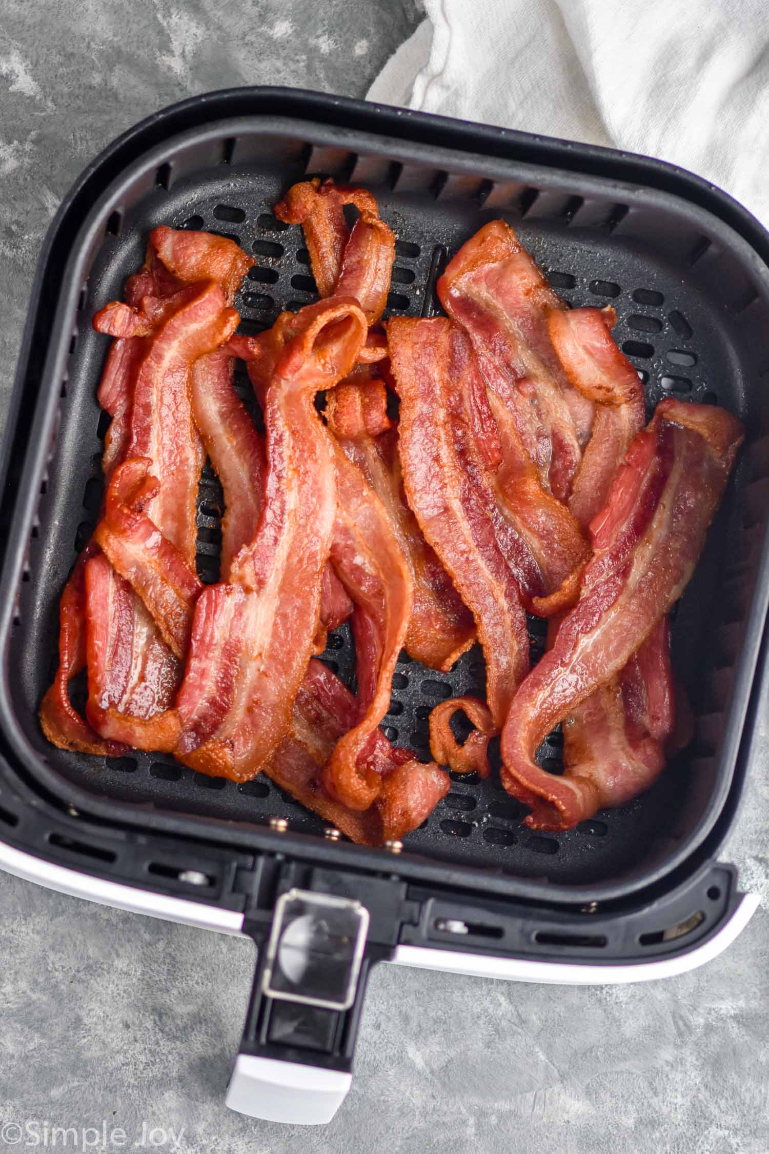 Overhead photo of cooked strips of bacon in air fryer basket for air fryer bacon.