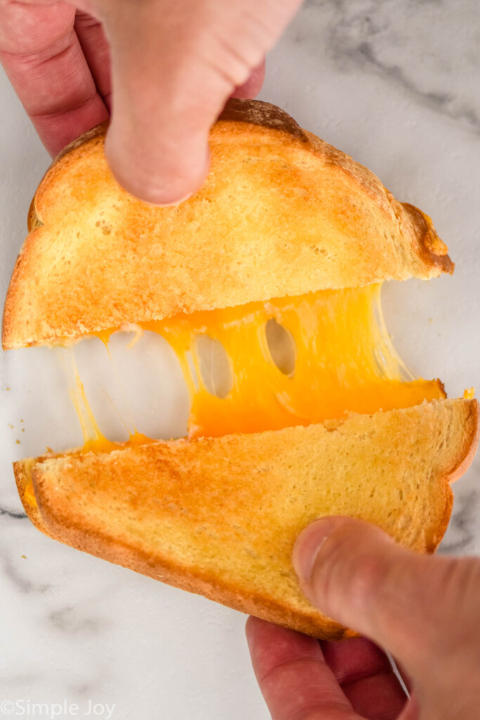 Overhead photo of man's hand pulling apart two halves of air fryer grilled cheese.