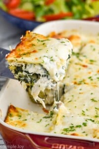 Overhead photo of spatula serving a slice of chicken alfredo lasagna from baking dish.