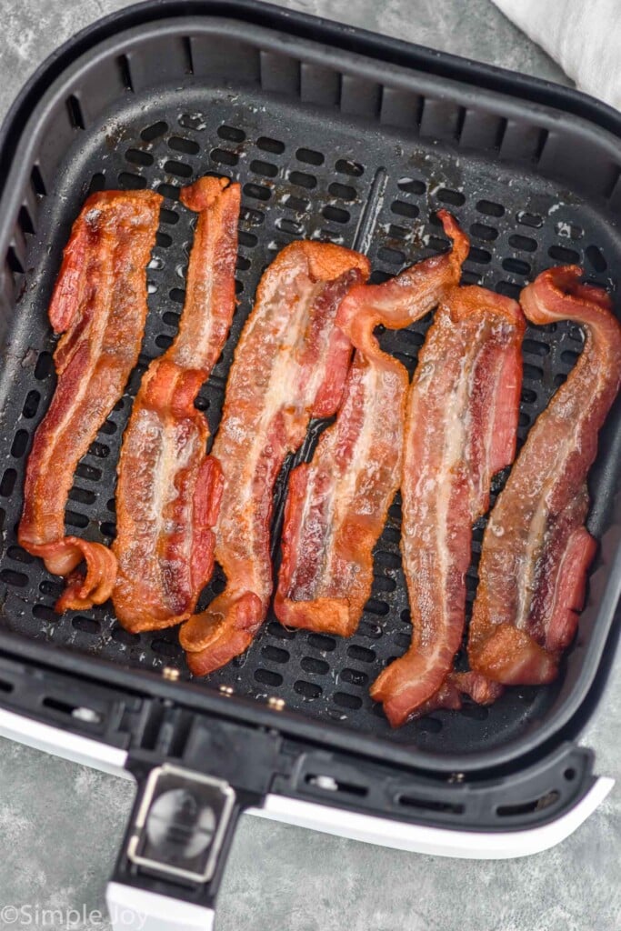 Overhead photo of cooked strips of bacon in air fryer basket for air fryer bacon.