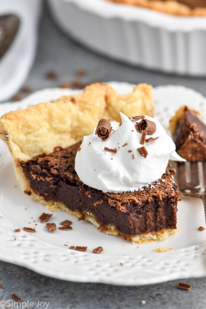 Overhead photo of slice of chocolate chess pie garnished with a dollop of whipped cream. Slice is served in a plate with a fork and has a piece taken off that is still resting on the fork.