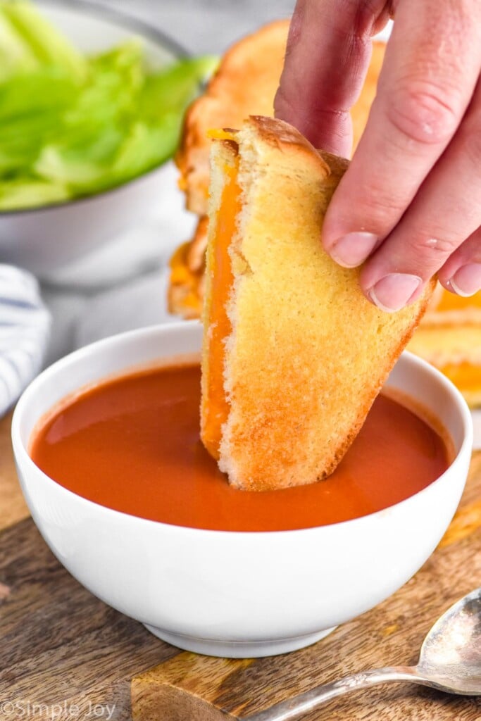Photo of man's hand dipping half of an air fryer grilled cheese sandwich into a bowl of tomato soup.