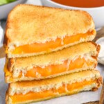 Photo of stack of air fryer grilled cheese sandwiches halves with a bowl of tomato soup behind them.