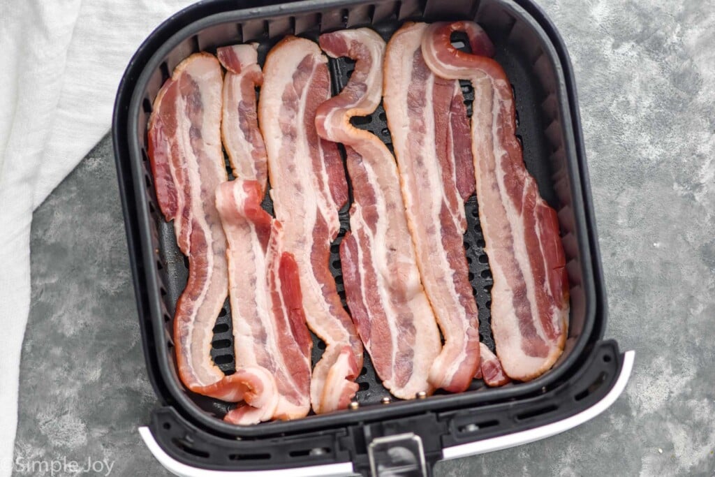 Overhead photo of strips of bacon in air fryer basket for air fryer bacon recipe.