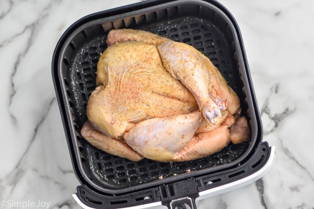 Overhead photo of chicken in an air fryer basket for air fryer whole chicken recipe.
