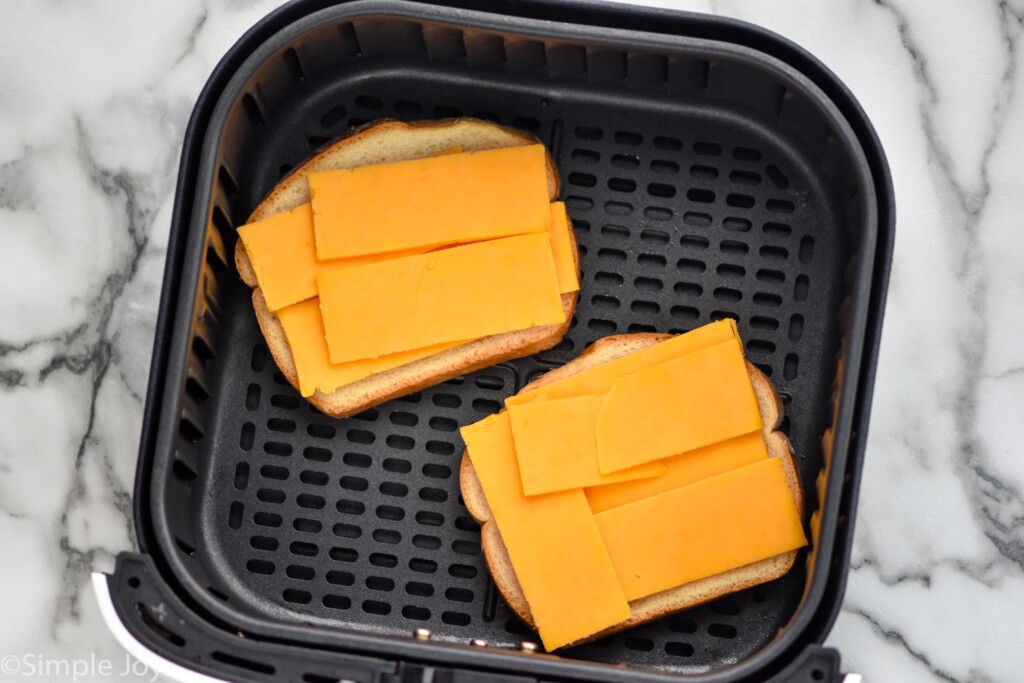 Overhead photo of bread and cheese in air fryer basket for air fryer grilled cheese recipe.