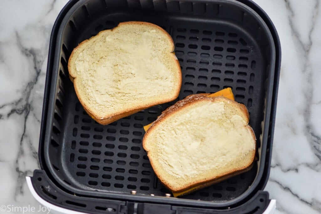 Overhead photo of air fryer grilled cheese sandwiches in an air fryer basket ready to be cooked.