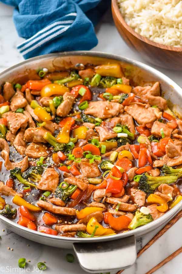 Overhead photo of pork stir fry in a pan. A bowl of rice sits on the counter beside the stir fry.