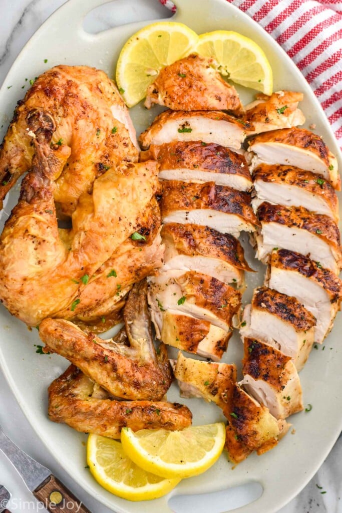 Overhead photo air fryer whole chicken recipe sliced and served on a tray with slices of lemon.