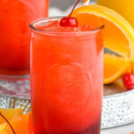 Photo of Alabama Slammer cocktails served in a glass garnished with orange slice and a cherry.