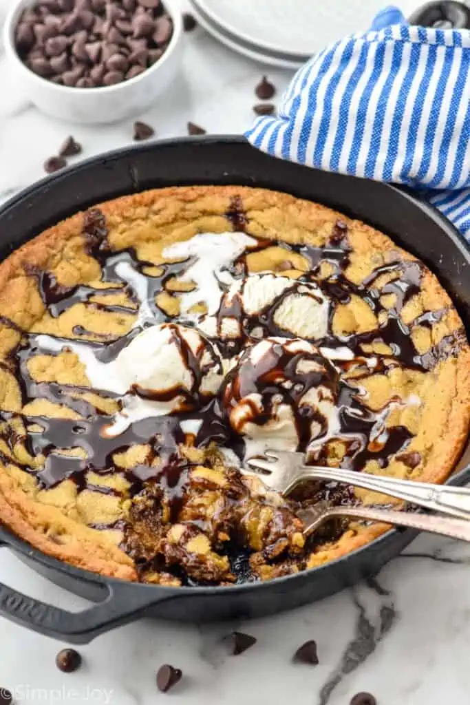 Overhead photo of Pizookie recipe garnished with ice cream and hot fudge sauce. Two forks are in the pizookie for eating.