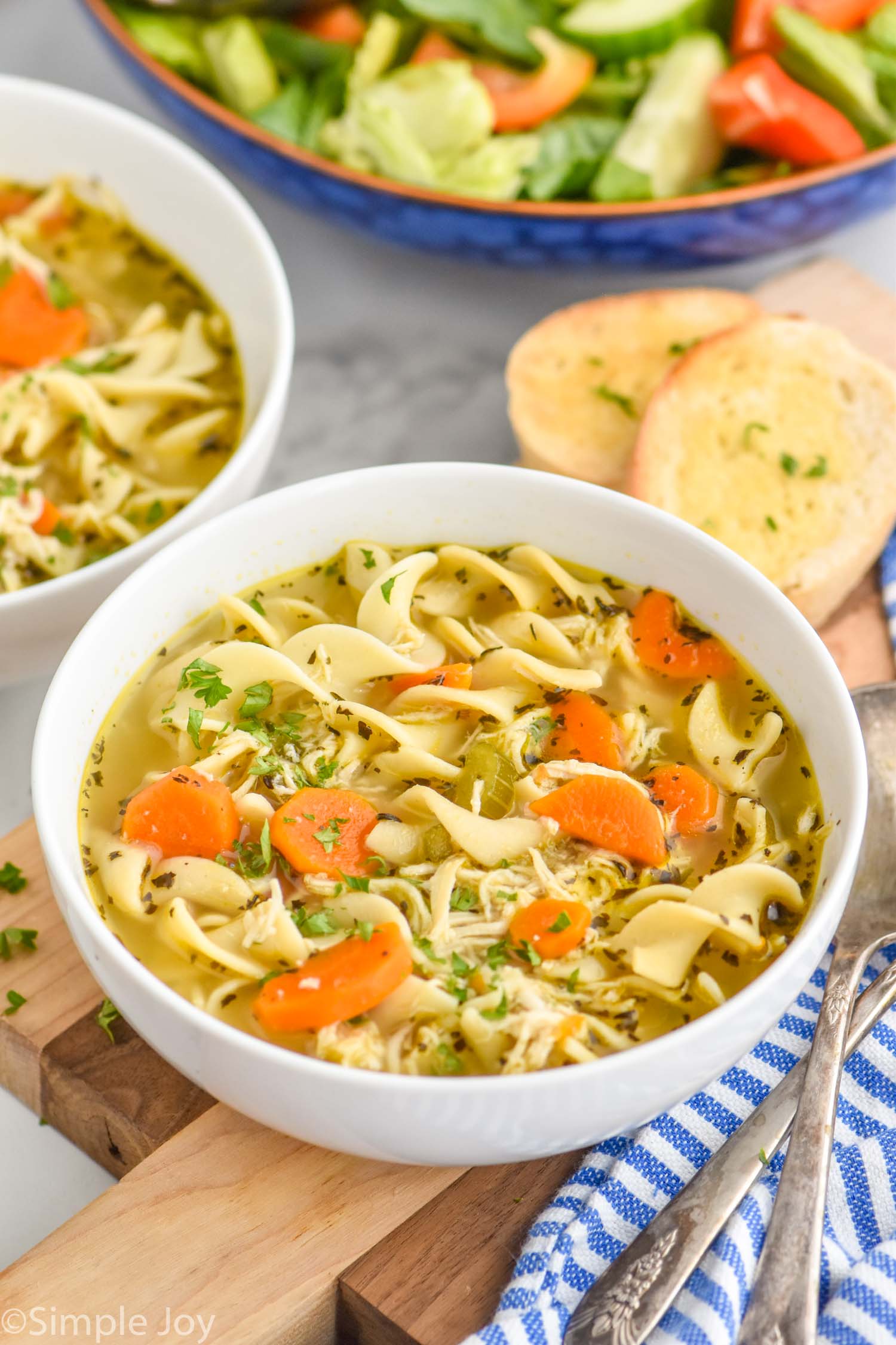 Overhead photo of Instant Pot Chicken Noodle Soup recipe in bowls for serving. Slices of bread beside bowls of soup.