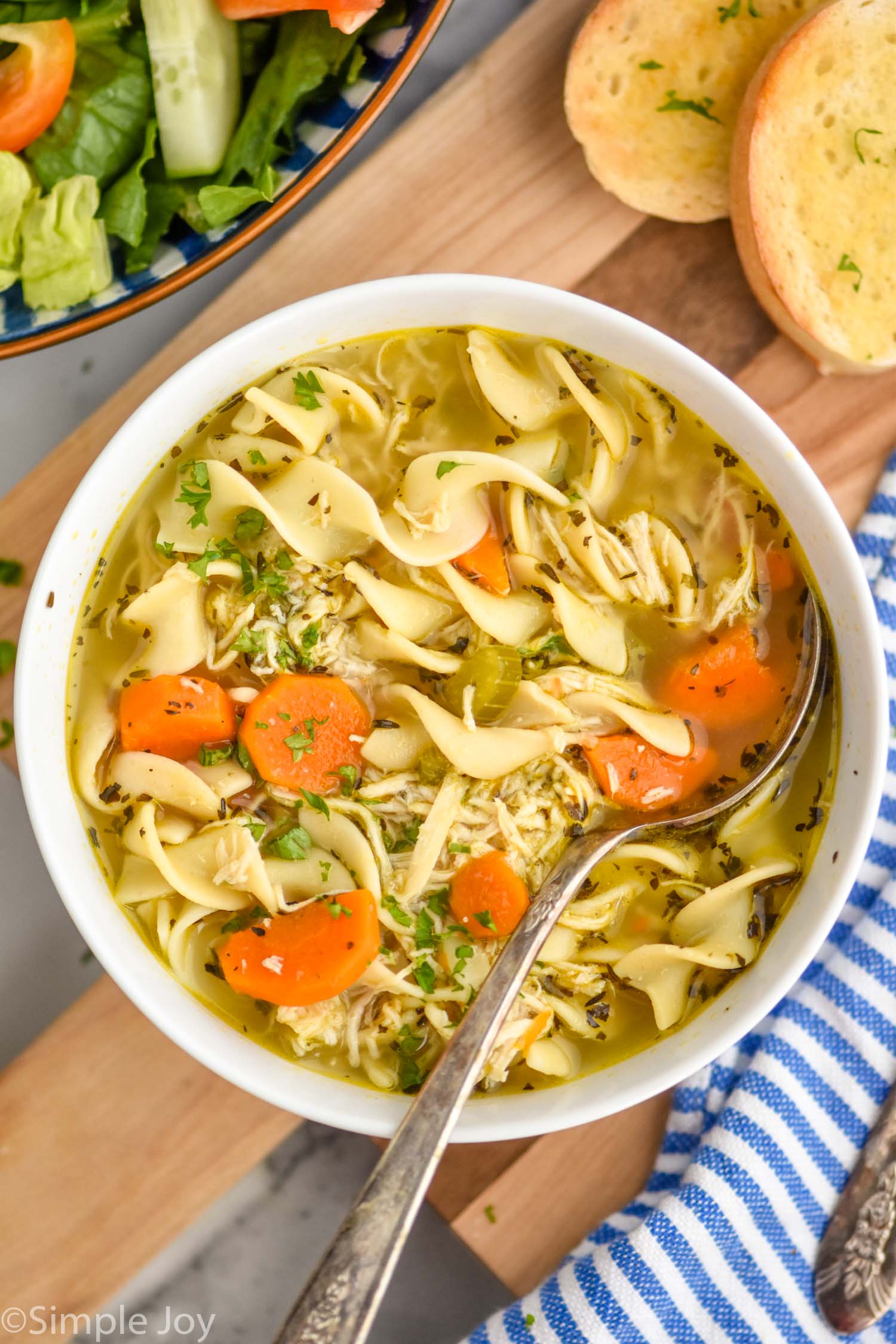 Overhead photo of Instant Pot Chicken Noodle Soup recipe in bowl with a metal spoon. Slices of bread beside bowls of soup.