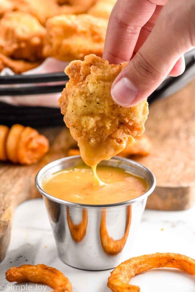 Photo of chicken nugget being dipped in dipping sauce by person's hand.
