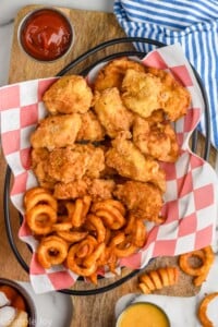 Overhead photo of chicken nuggets recipe in a basket with curly fries and a side of ketchup.