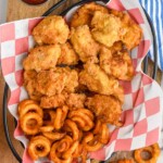Overhead photo of chicken nuggets recipe in a basket with curly fries and a side of ketchup.
